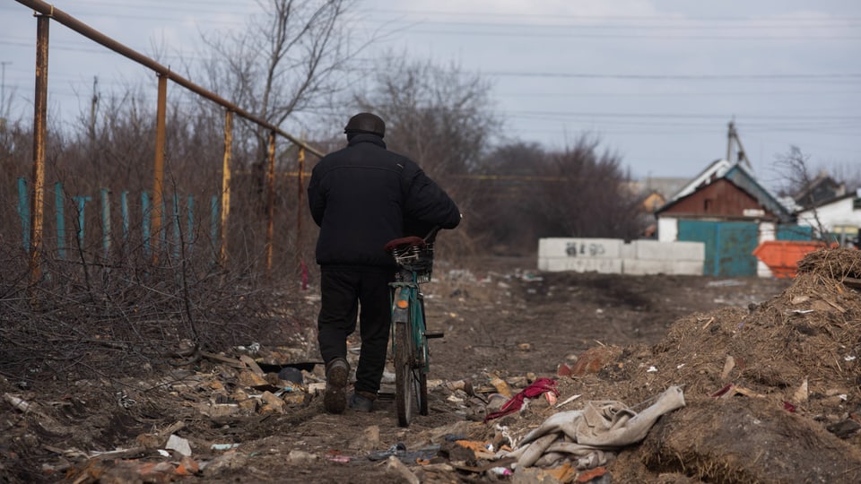 Ein Mann läuft mit einem Fahrrad durch eine zerstörte Gegend in der Ukraine. 