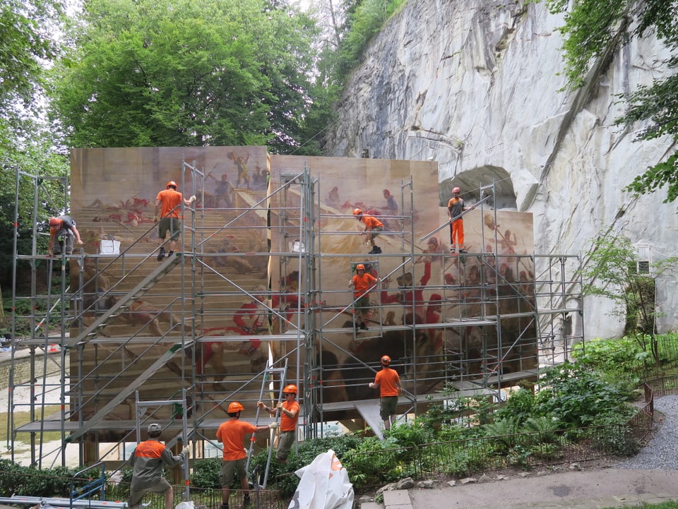 Arbeiter bei der Montage eines riesigen Wandgemäldes vor einem Felsen. 