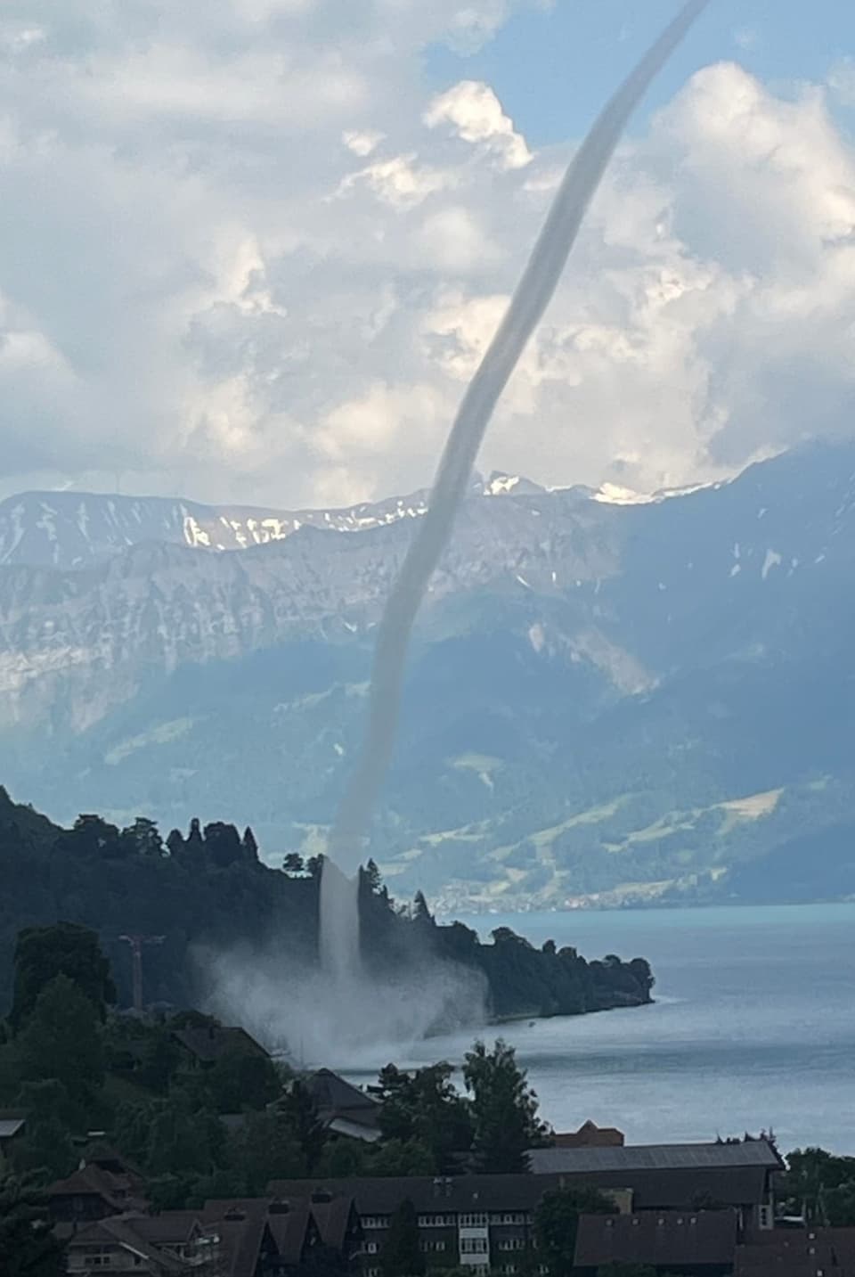 Blick auf See mit Ufer. Über dem Wasser dreht ein Schlauch, der sich bis in die Wolken hochzieht. 