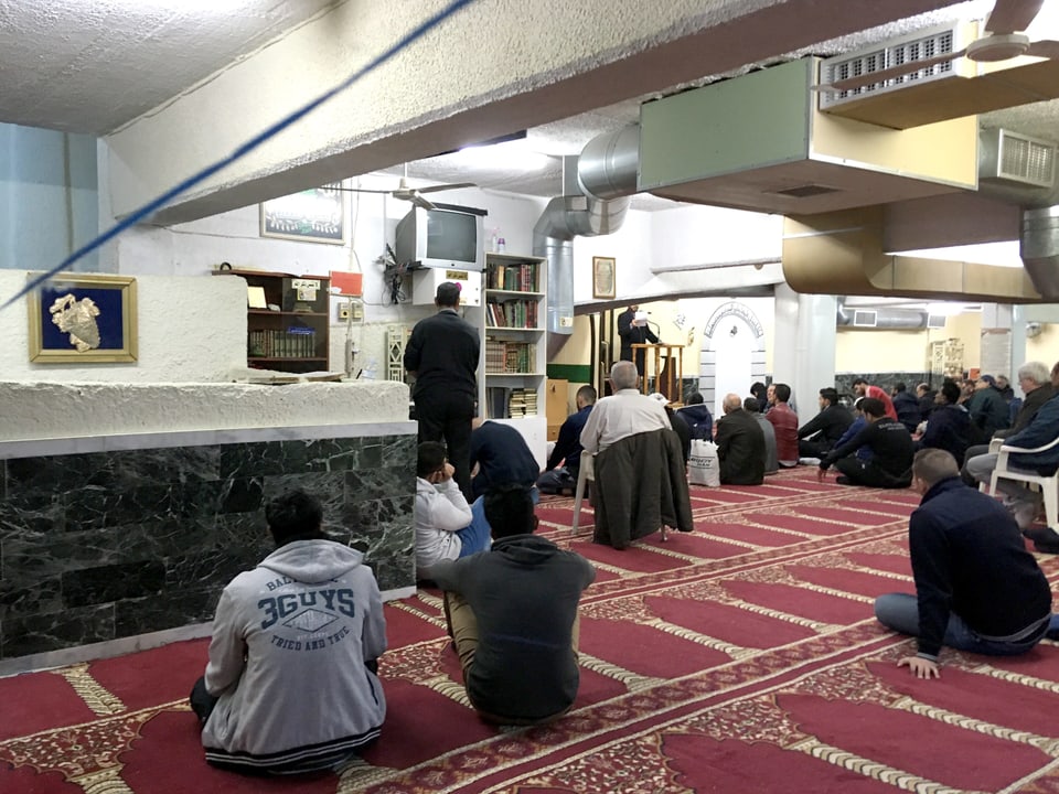 Männer sitzen auf dem Boden in einer Kellerwohnung und nehmen an einem Gebet teil