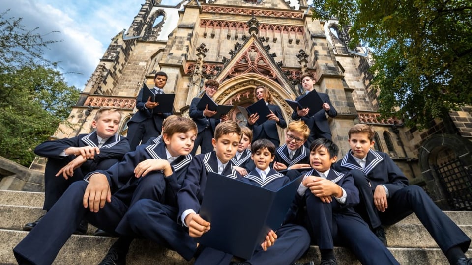Eine Gruppe von Jungen mit Notenordner und einheitlicher Choruniform vor einer gotischen Kirche.