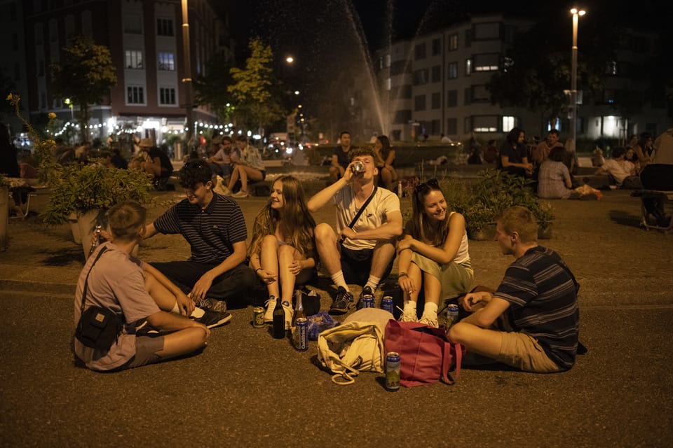 Eine Gruppe sitzt spät in der Nacht auf einem Platz in Zürich, trinkt und redet.