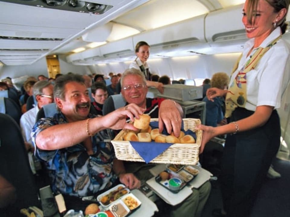 Eine Stewardess serviert zwei Reisenden das Mittagessen auf einem Flug. 