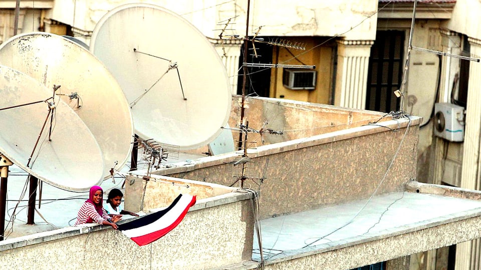 Zwei Mursi-Anhängerinnen auf einem Dach rollen die ägyptische Nationalflagge aus.