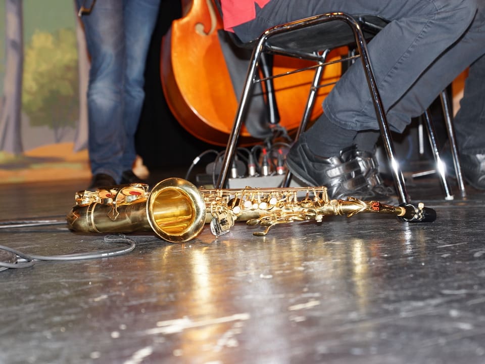 Ein goldenes Saxofon liegt vor einem Musiker auf dem Boden.