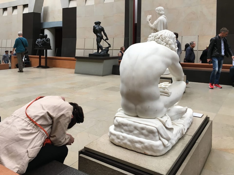 Frau sitzt neben einer Marmor-Skulptur im Musem