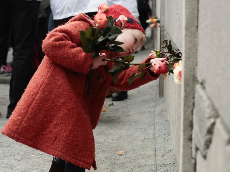 Mädchen legt Blumen in die Mauer.