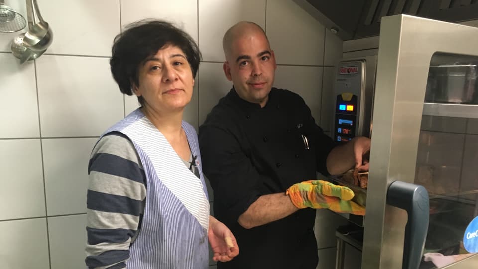 Eine kurdische Frau und ein männlicher Koch werken in einer Küche. 