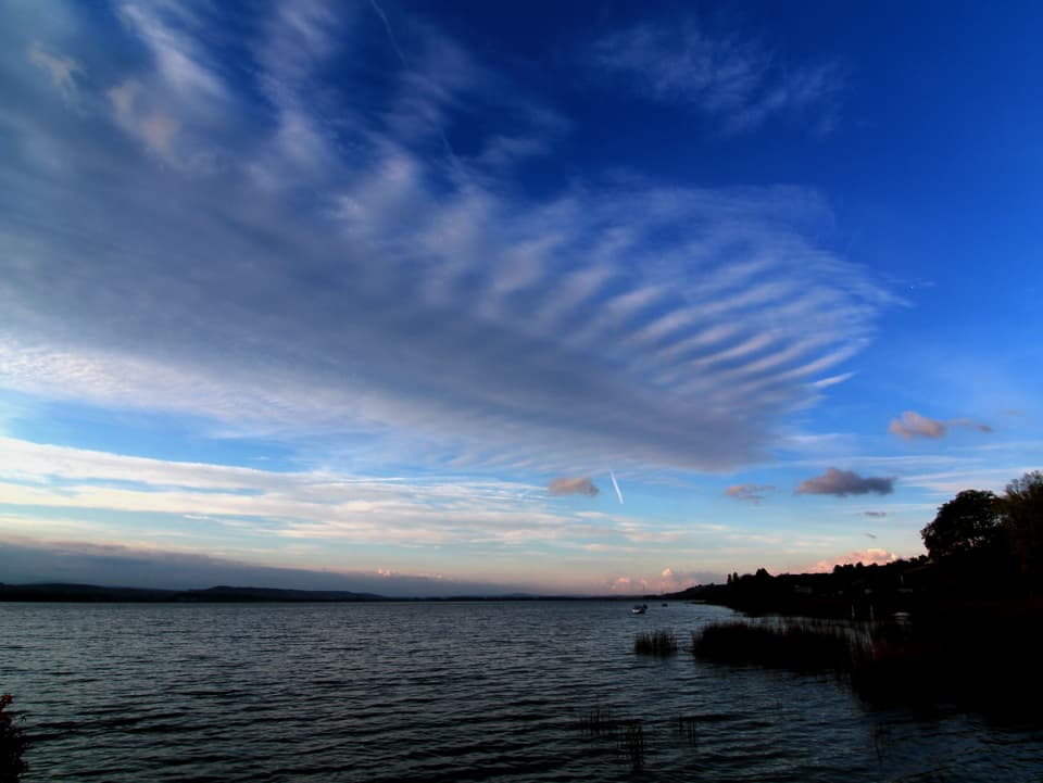 Ein Band aus Wolken mit Wellenform am sonst blauen Himmel. Darunter liegt ein See.