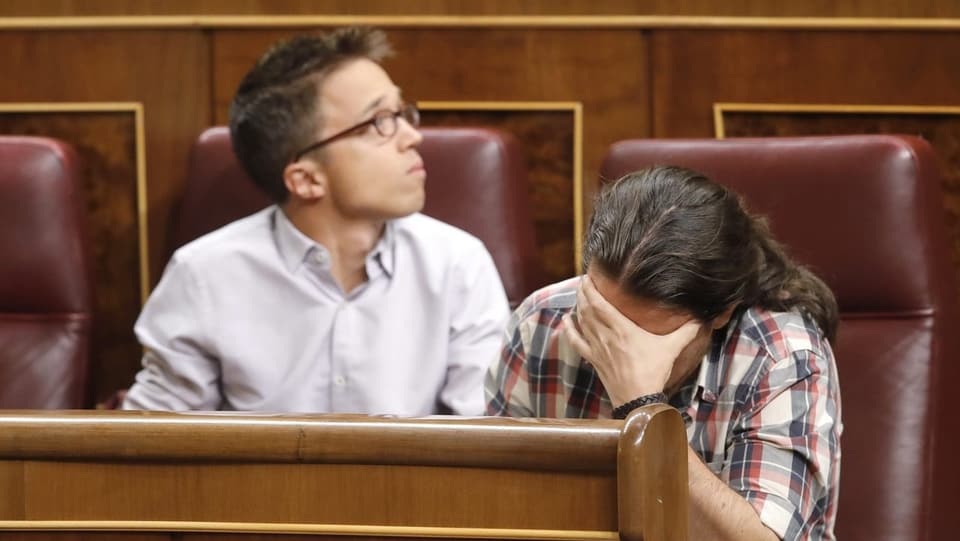 Pablo Iglesias hät sich im Parlament sitzend die Hand vors Gesicht. Sein Sprecher Inigo Errejon sitzt daneben. 
