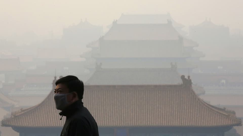 Ein Mann mit einer Atemschutzmaske, im Hintergrund Dächer einer Stadt.