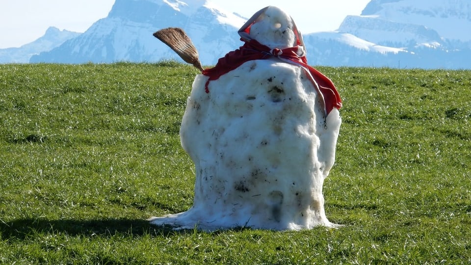 Eine Schneefrau auf einer grüne Wiese.