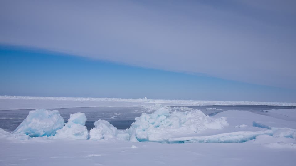 Blick über den gefrorenen arktischen Ozean mit Packeis im Vordergrund.