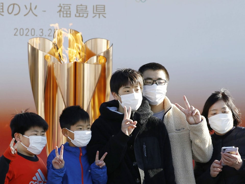 Menschen posieren vor der olympischen Flamme in Tokio.