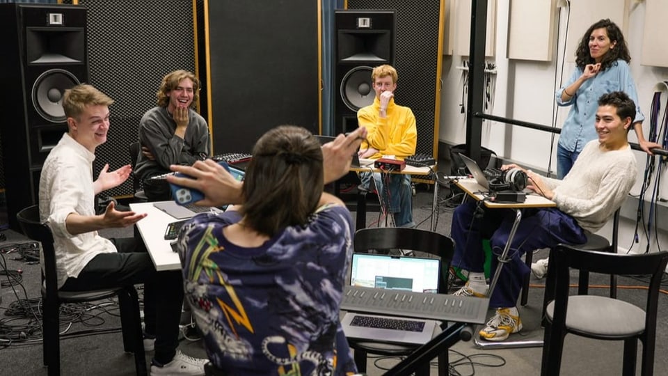 Eine Gruppe junger Menschen sitzt im Kreis in einem Tonstudio.