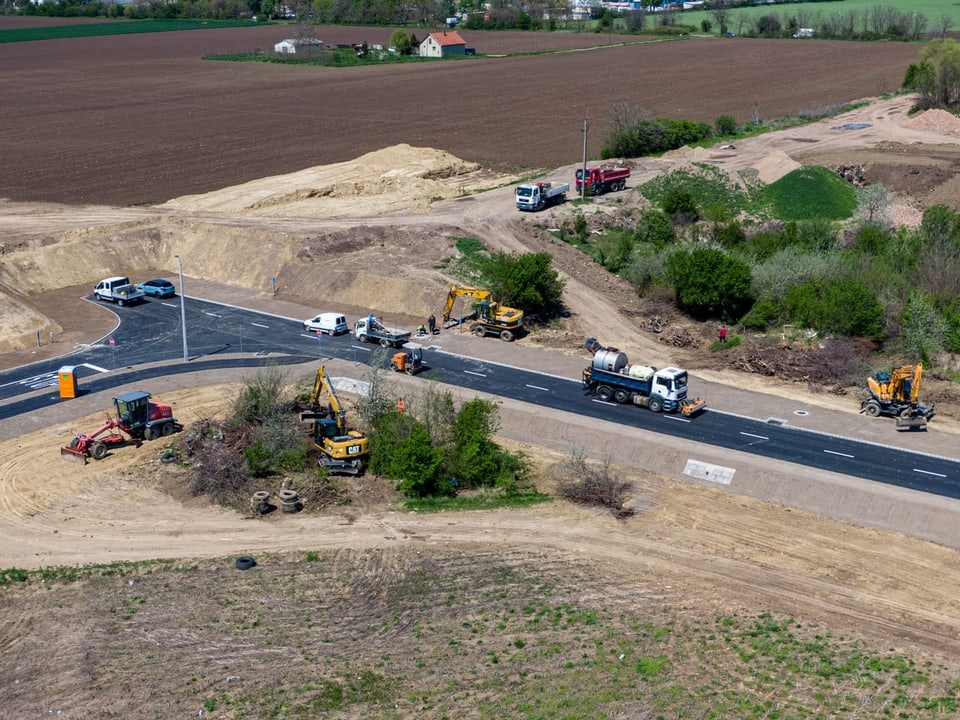 Eine neue Strasse in der Landschaft. Baumaschinen stehen herum. Sie endet an einem Erdwall.