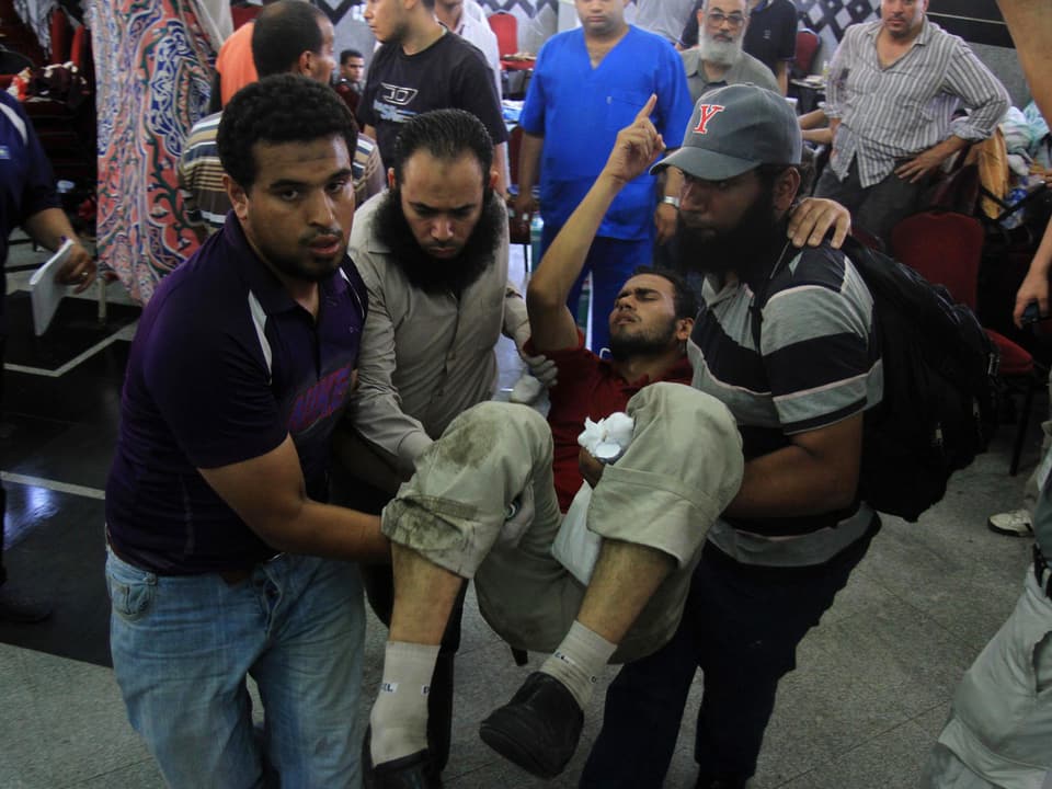 Muslimbrüder tragen nach den Zusammenstössen in Kairo einen Verletzten durch die Menschenmenge.