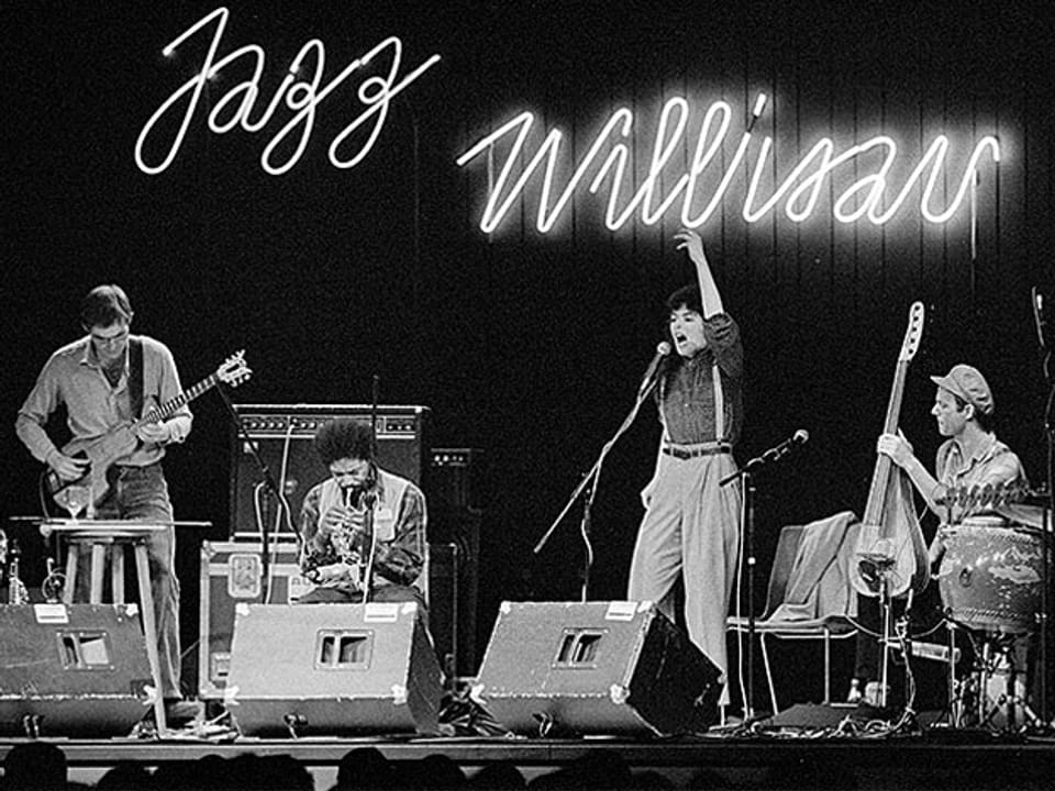 Totalaufnahme der Bühne mit der Leutschrift "Jazz Willisau" im Hintergrund, Shelley Hirsch singt mit erhobenem Arm.