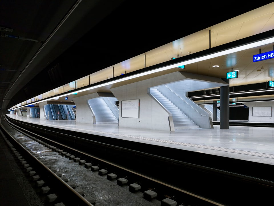 Blick auf ein unterirdisches Bahngeleise in warmen Farbtönen mit Leuchttafel «Zürich HB».