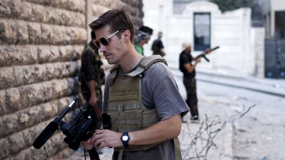 Kriegsreporter Foley mit einer TV-Kamera im Vordergrund – im Hintergrund ein Rebell mit einer Maschinenpistole.