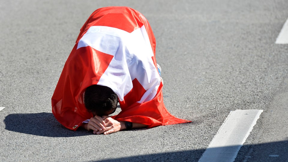 Viktor Röthlin, eingehüllt in die Schweizer Fahne, kniet am Boden.