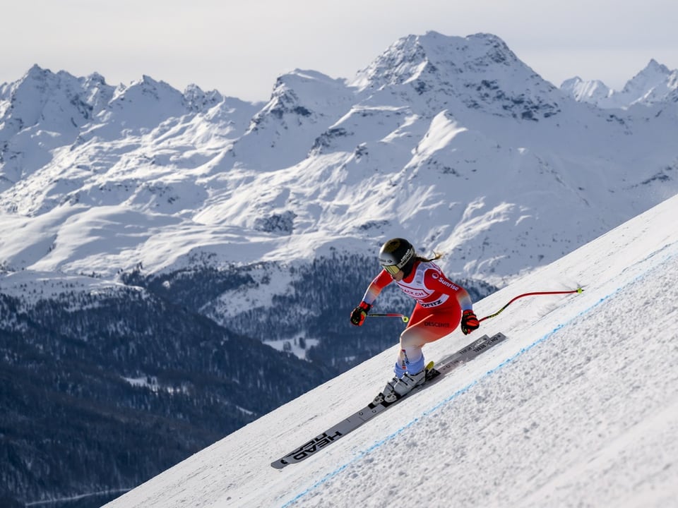 Skifahrer bei der Abfahrt auf einer verschneiten Piste mit Bergpanorama im Hintergrund