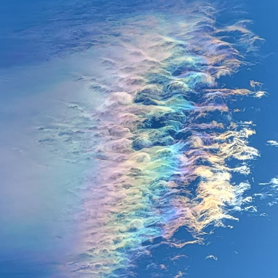 Andermatt/UR Dünne Eiskristallwolke am blauen Himmel, die wie ein Regenbogen leuchtet.