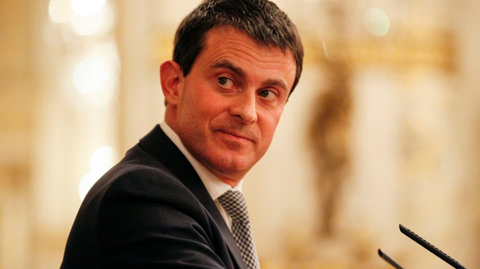 Valls blickt vor einem Mikrofon rechts über die Schulter zurück.