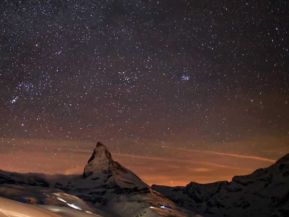 Nacht mit Sternenhimmel. Unten ein pyramidenförmiger Berg, das Matterhorn. 
