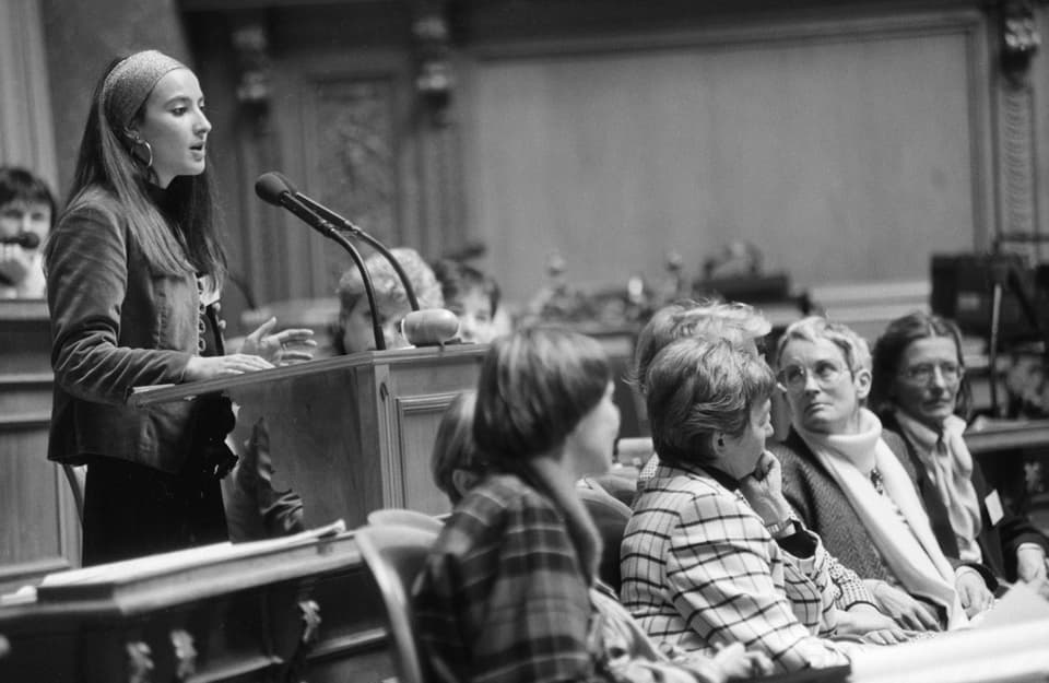 Eine Frau spricht am Rednerpult im Bundeshaus, andere verfolgen die Debatte.