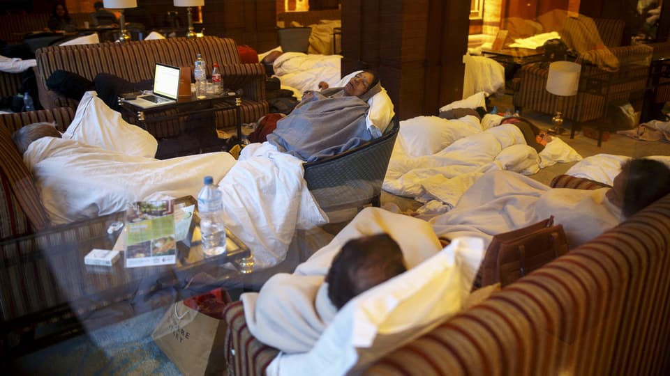 Touristen schlafen auf Sesseln in einer Hotelhalle.