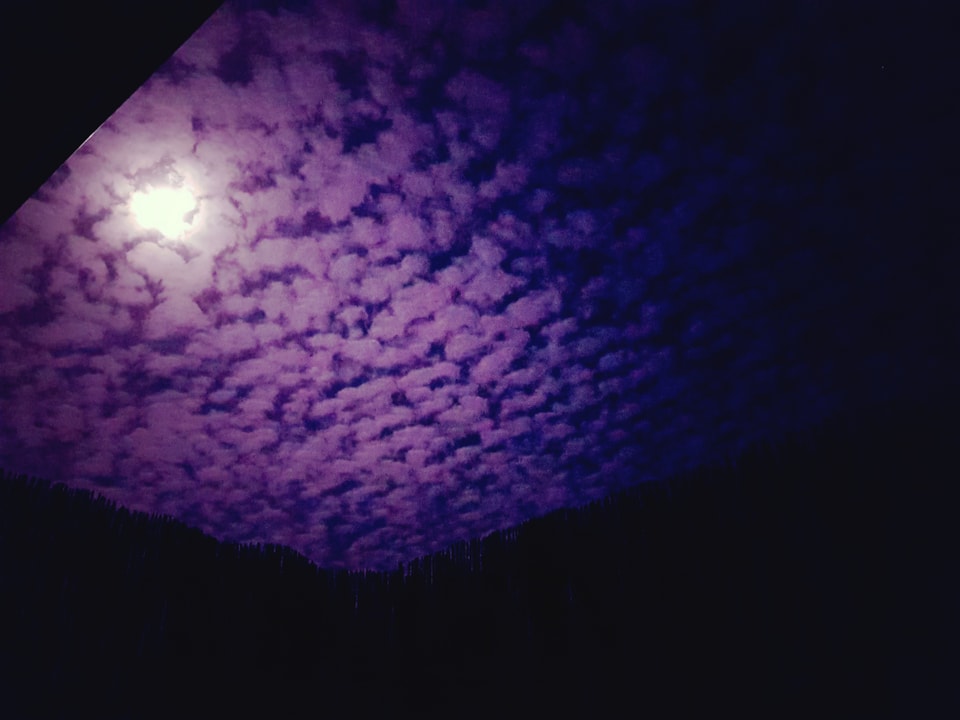 Violette Schäfchenwolken am Nachthimmel mit Mond.