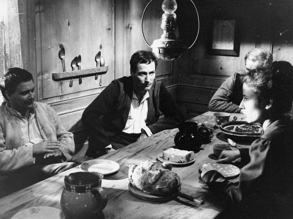 Drei Männer und eine Frau sitzen beim Abendbrot am Tisch. 