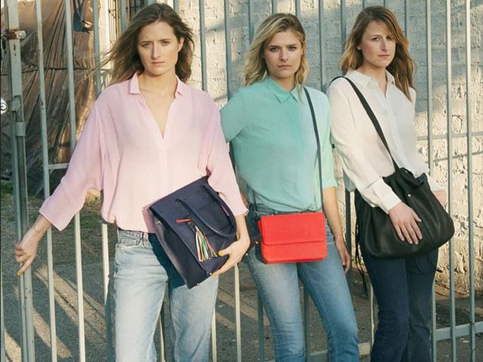 Drei junge Freuen mit Handtaschen nebeneinander stehend.