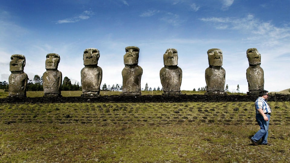 Moai in einer Reihe, davor ein Tourist.