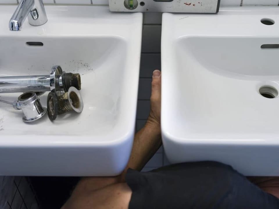 Zwei lavabos, dazwischen die Hände eines handwerkers, der die Lavabos einbaut. 