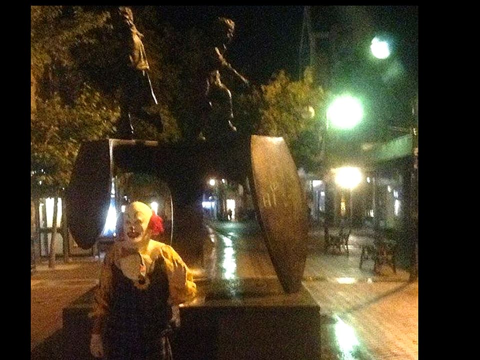 Clown vor Skulptur stehend
