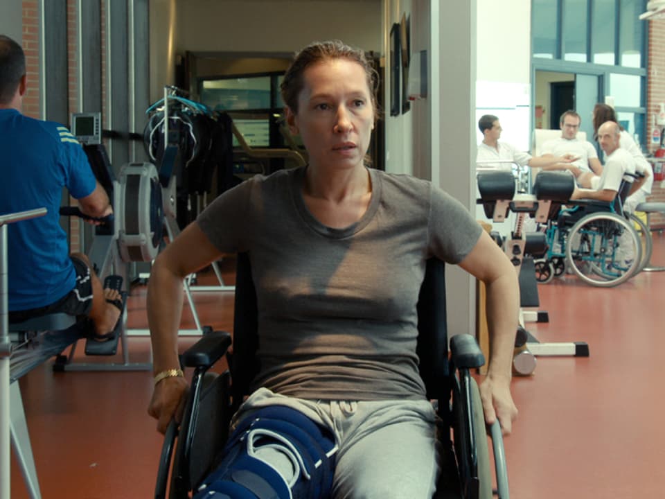 Eine Frau sitzt im Rollstuhl in einem Raum mit Rehabilitationsgeräten.