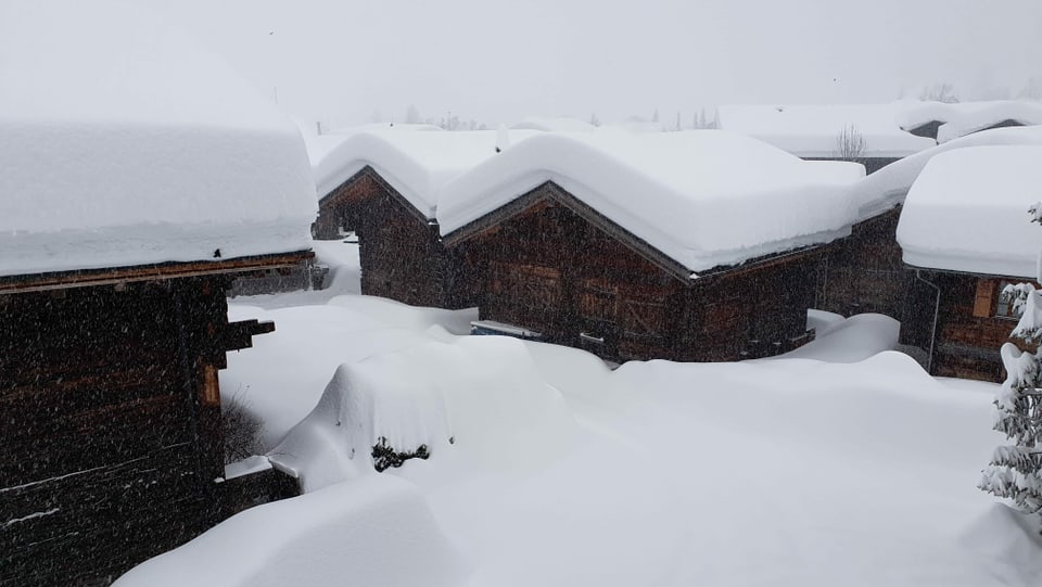 Eine Gruppe von Holzhäusern mit riesigen Schneemengen auf den Dächern.