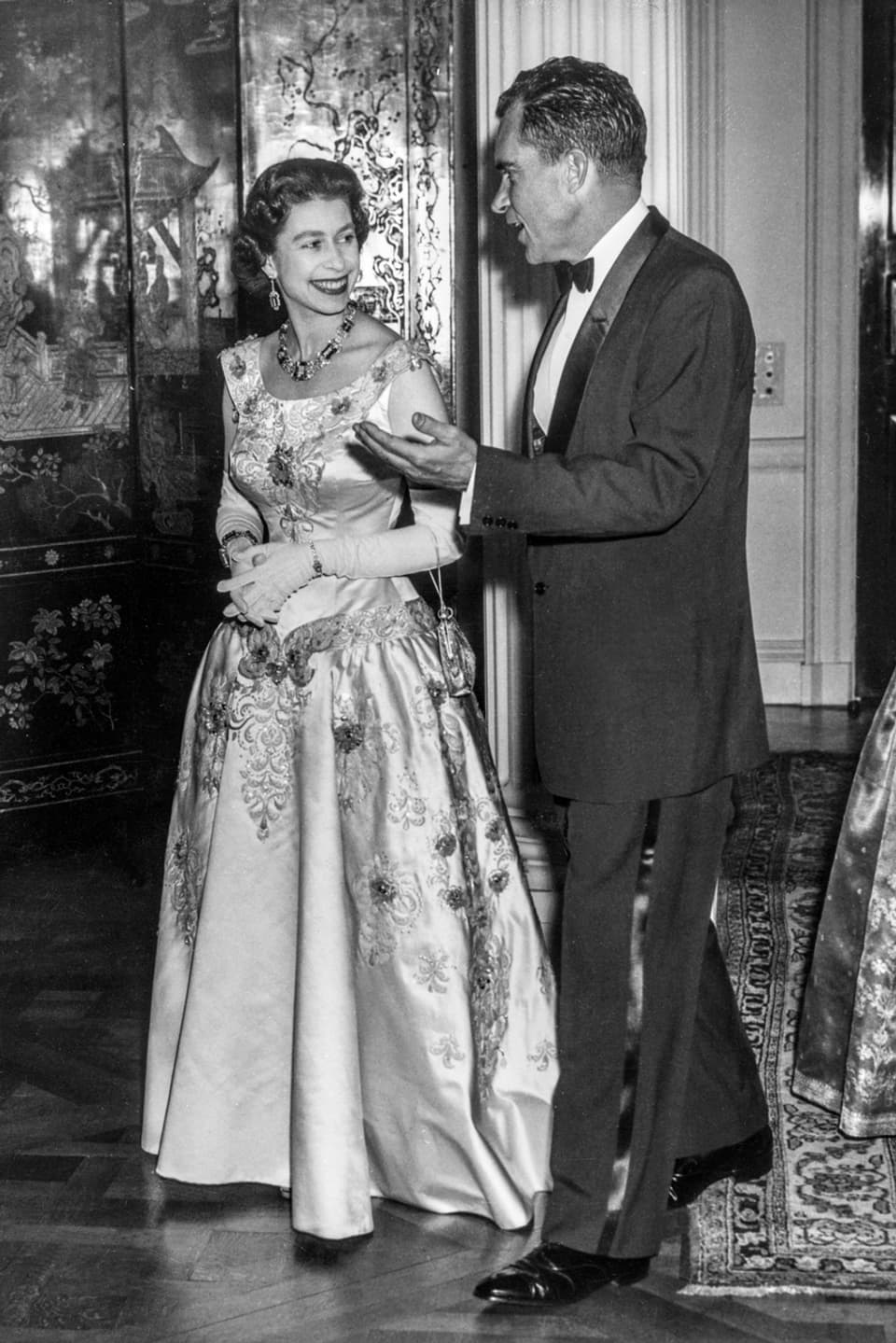 Die junge Queen Elisabeth in einem wunderschönen Ballkleid und Handschuhen. Neben ihr steht Richard Nixon.