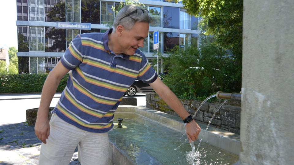 Ein Mann hält die Smartwatch Pebble an einem Brunnen unter das fliessende Wasser.