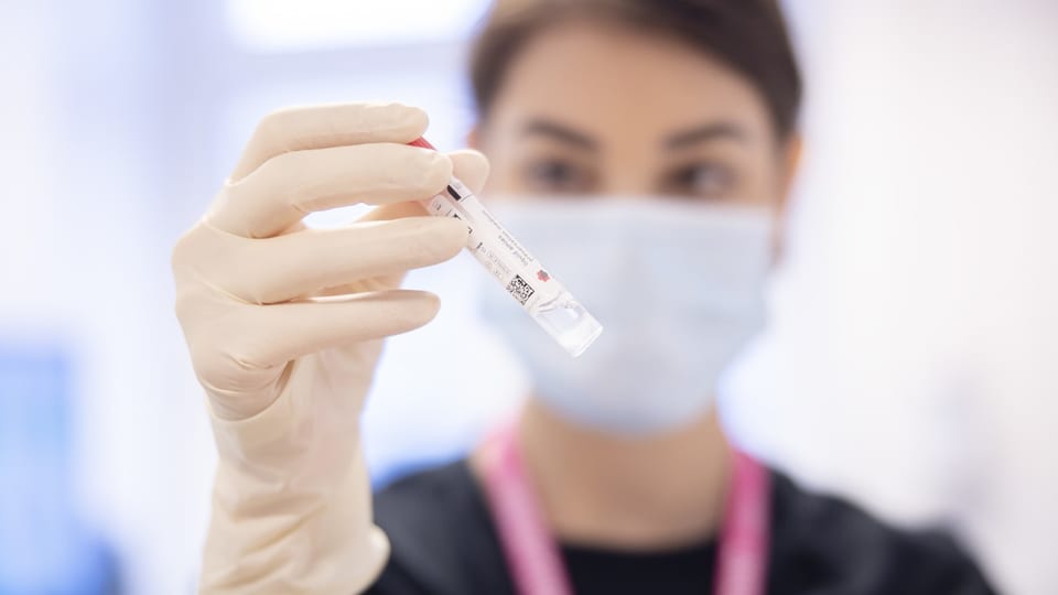 Medizinische Fachkraft in einem Mundschutz hält eine Reagenzglasprobe im Labor.