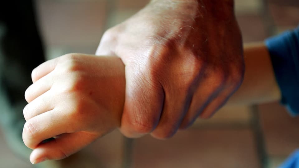Eine starke Männerhand greift nach einem Kinderarm (Symbolbild).