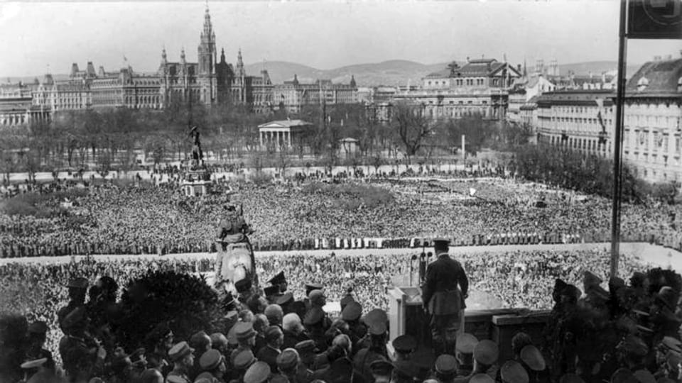 Schwarz-weiss Aufnahme mit Hitler von hinten im Vordergrund und einer Menschenmasse im Hintergrund.