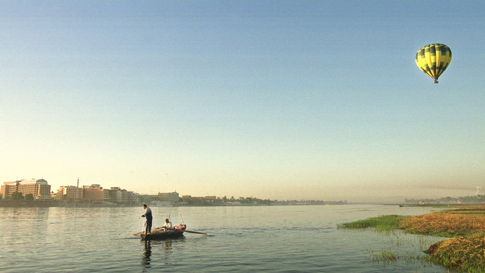 Ein Fischerboot treibt auf dem Nil, darüber ein Heissluftballon.