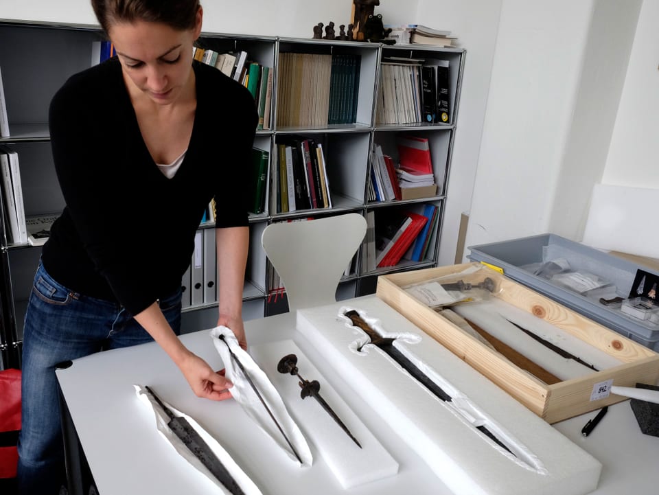 Die Archäologin Anette JeanRichard steht an einem Tisch und zeigt die Morgarten-Funde und andere Waffen.