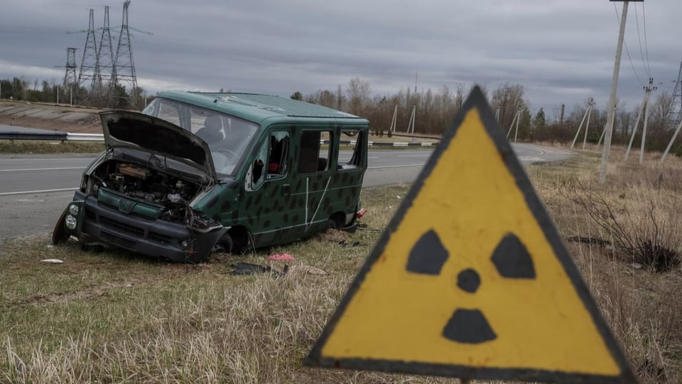 Zerstörtes Auto und Schild mit radioaktivitätszeichen.