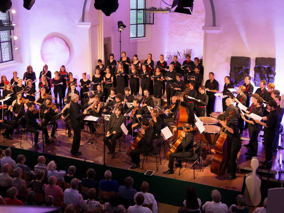 Die Sängerinnen, Sänger und Musiker auf der Bühne in einem Kirchenschiff.