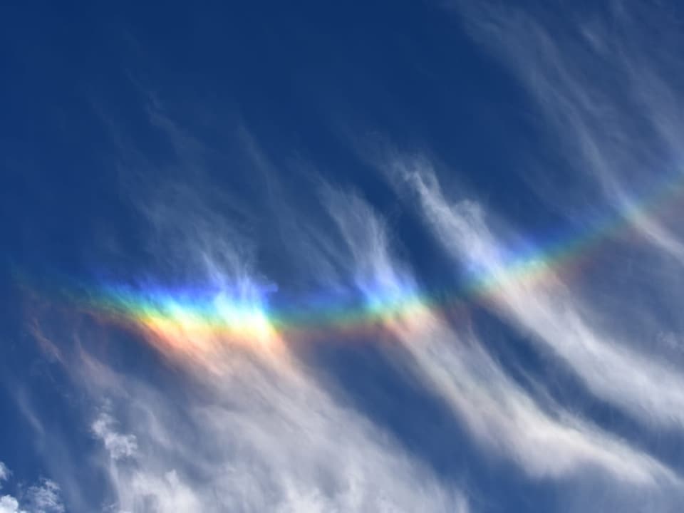 Blauer Himmel mit Schleierwolken, in der Mitte des Bildes leuchten die Wolken in allen Regenbogenfarben.