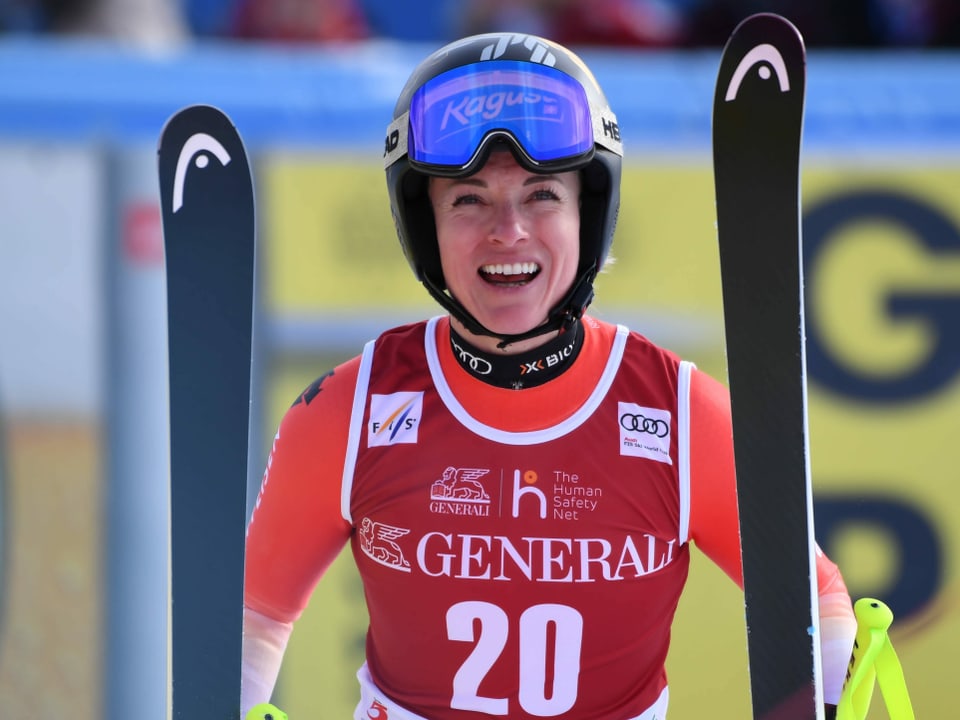 Lara Gut-Behrami lächelt mit je einem Ski in der Hand.
